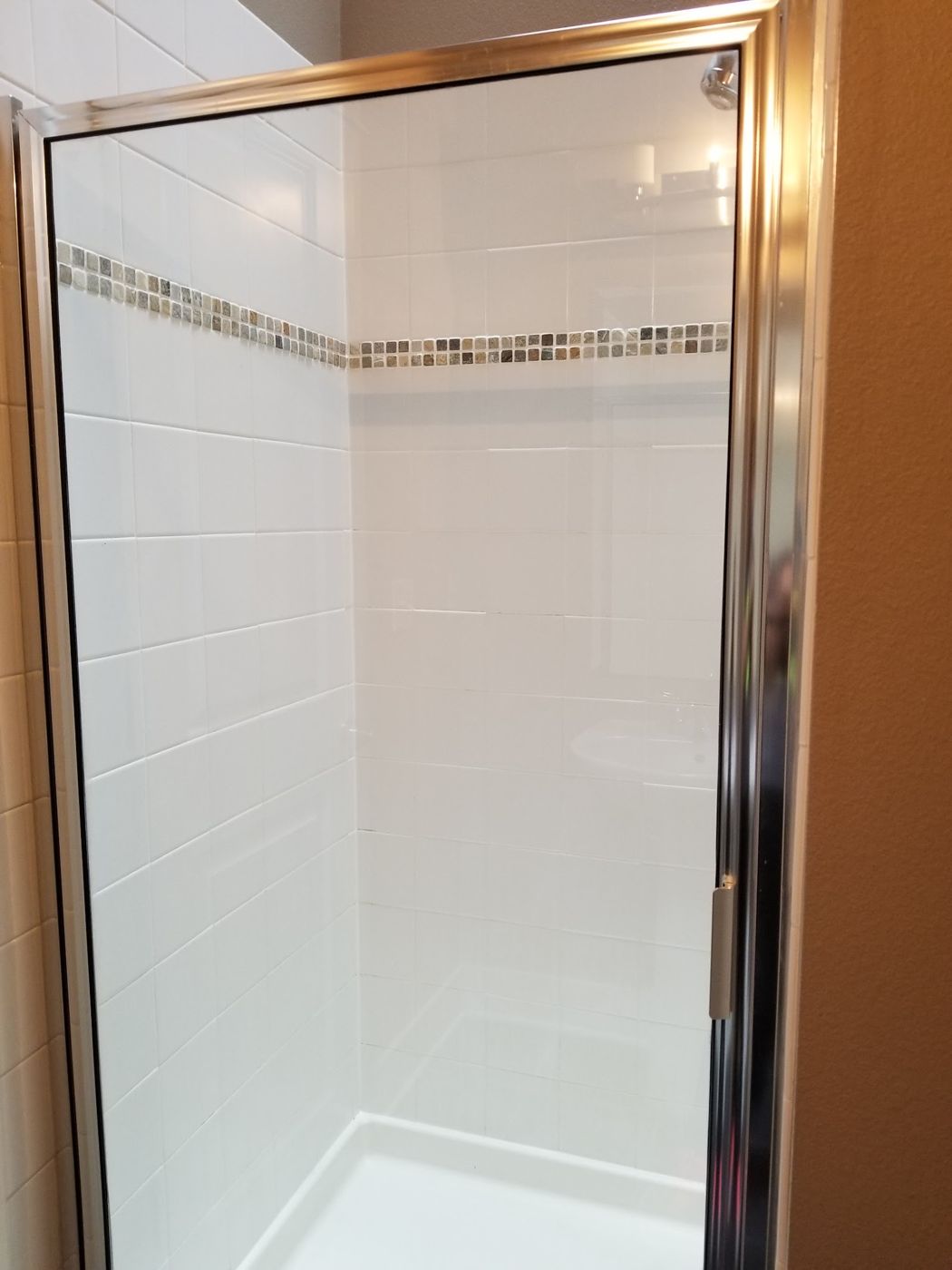 Clean glass-door shower stall with white tile and accent band